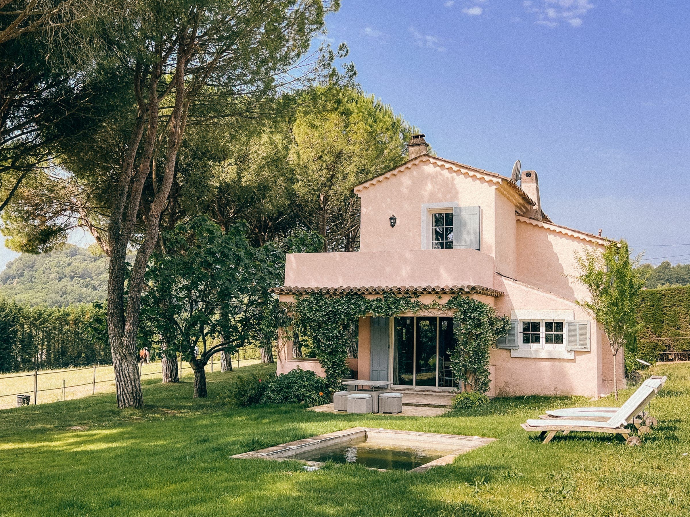 The pink Provençal house of Le Mas Rose among pine trees, with lawn and sun loungers